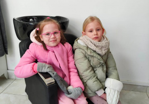 Dwie dziewczynki siedzą na fotelu w salonie fryzjerskim
