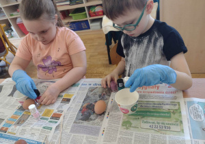 Dwoje dzieci z grupy piątej maluje jajka lakierem