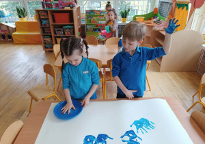 Dwoje dzieci z grupy trzeciej maluje swoje ręce na niebiesko