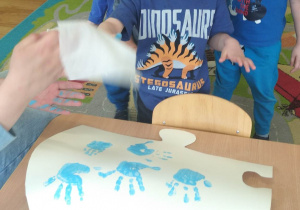 Dzieci z grupy pierwszej odbijają swoje dłonie umoczone w niebieskiej farbie
