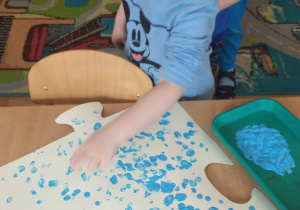 Chłopiec stawia niebieskie kropki namoczonym palcem w niebieskiej farbie