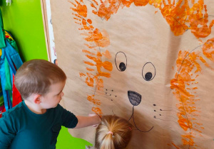 Dzieci robią grzywę lwu za pomocą swoich rąk pomalowanych farbą