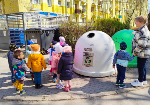 Dzieci z grupy pierwszej na spacerze uczą się kolorów pojemników na śmieci