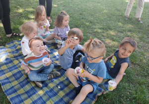 Dzieci siedzą na kocyku i jedzą lody