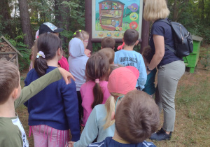 Nauczycielka odczytuje dzieciom tablice edukacyjną "Z wizytą w ulu"