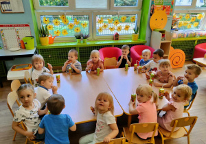 Dzieci z grupy I siedzą razem przy stolikach i piją soczki oraz jedzą słodkie misie