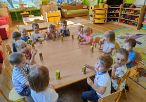 Dzieci z grupy I siedzą razem przy stolikach i piją soczki oraz jedzą słodkie misie