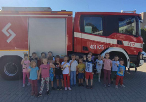 Przedszkolaki pozują do zdjęcia przed wozem strażackim