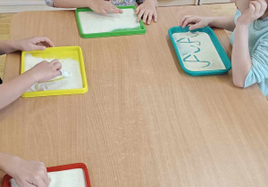 Dzieci piszą litery na tacy z kaszą