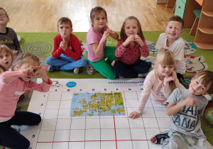 Przedszkolaki siedzą wokół maty, na której ułożyły mapę Europy