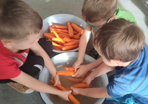 Trzech chłopców myje marchewkę w misce z wodą