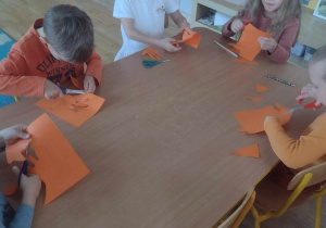 Piątka przedszkolaków z grupy V wycina swoje odrysowane dłonie na pomarańćzowej kartce