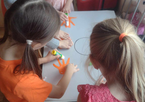 Czworo dzieci z grupy V przykleja swoje wycięte z pomarańczowego papieru dłonie na plakacie