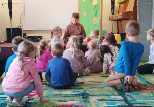 Dzieci słuchają książki czytanej przez absolwenta przedszkola