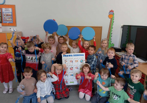 Dzieci z grupy II z niebieskimi wstążeczkami oraz tablicą z rozpisanymi prawami dziecka