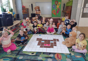 Dzieci z grupy piątej siedzą wokół ułożonego misia z kartoników na macie do kodowania