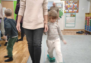 Dziewczynka w butach dinozaura idzie za rękę z mamą