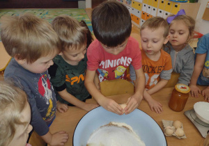 Dzieci patrzą jak chłopiec rozbija jajko do miski
