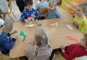 Dzieci siedzą przy stoliku z kolorowymi papierowymi paskami