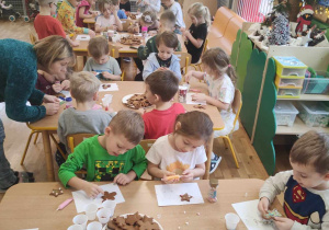 Dzieci z grupy trzeciej siedzą przy stolikach i ozdabiają pierniki