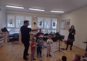 Troje dzieci z maluszków gra na instrumentach perkusyjnych podczas śpiewania piosenki