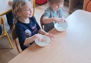 Dwie dziewczynki bawią się mąką w miseczkach