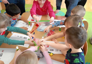 Dzieci przyklejają skrawki rózńych materiałów na kartkę