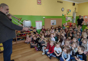 Dzieci słuchają jak pan gra na puzonie
