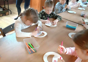 Dzieci robią przy stolikach koszyczki wielkanocne z papierowych talerzyków